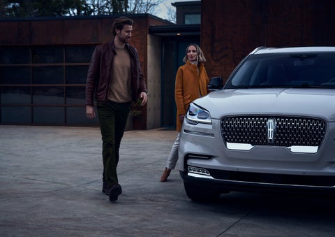 A man and a woman approaching a 2024 Lincoln Aviator® SUV, which illuminates certain lights when they are close | Lidtke Lincoln in Beaver Dam WI