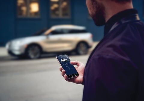 A person is shown interacting with a smartphone to connect to a Lincoln vehicle across the street. | Lidtke Lincoln in Beaver Dam WI